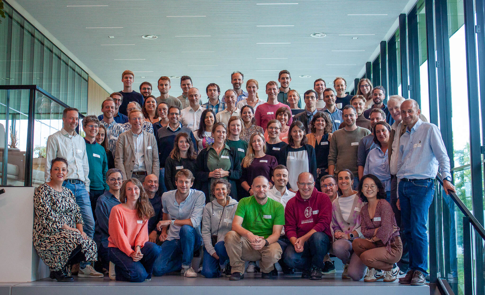 A group of people smiling and posing for a photo in front of a large window with natural light streaming in.