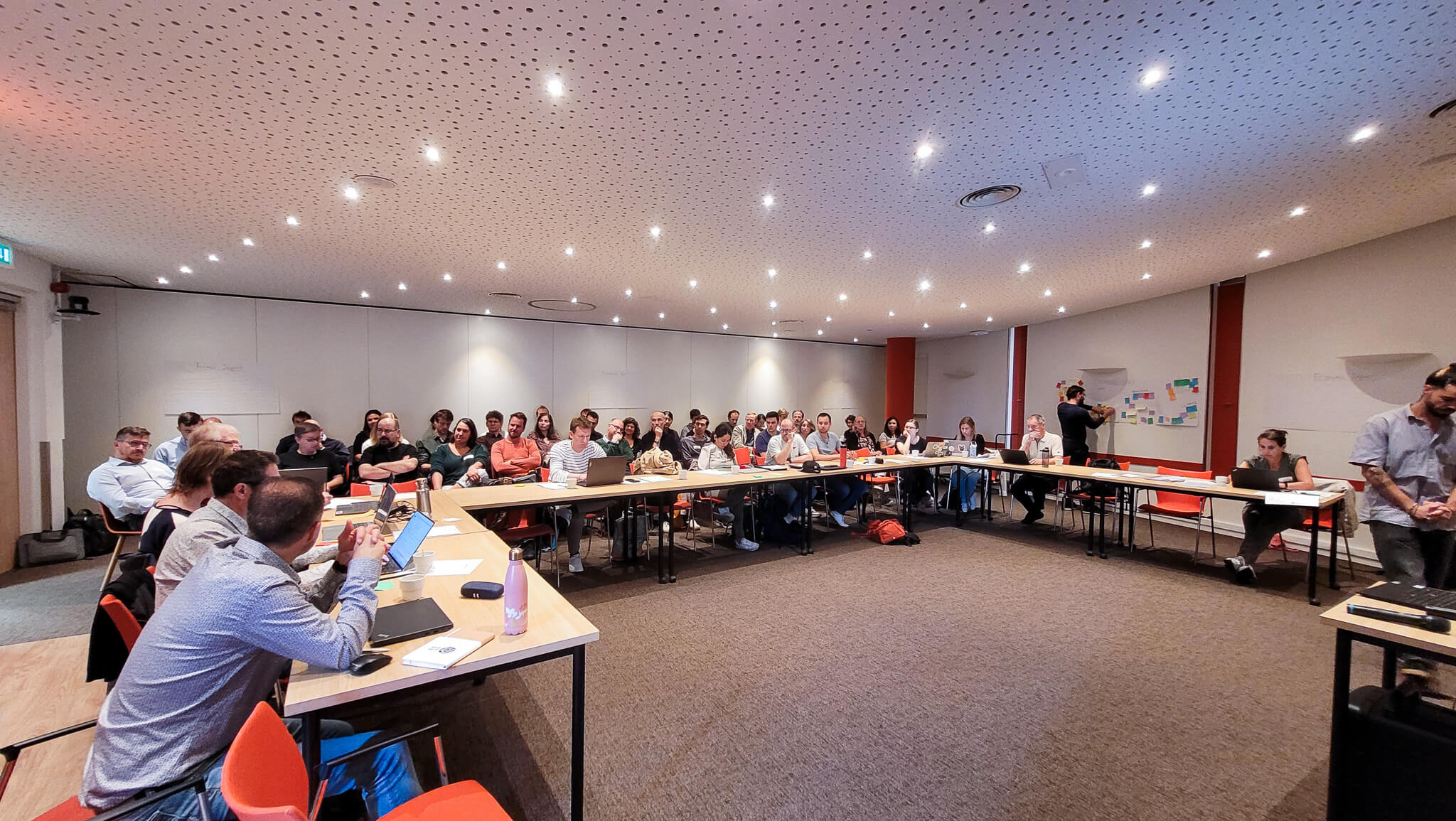A group of people seated at tables in a well-lit room, engaged in conversation and activities.