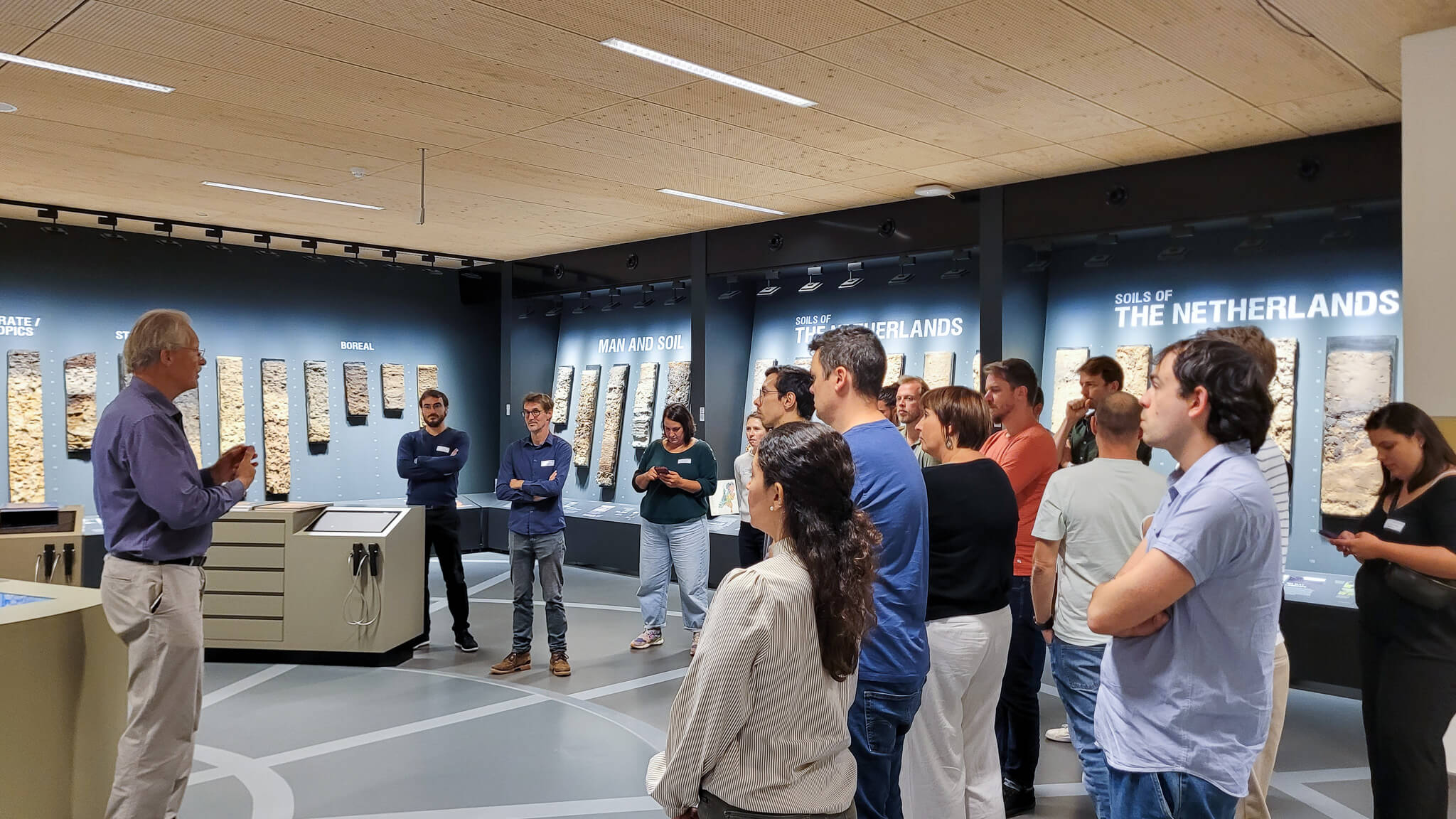 A group of people stands in a museum, observing various artifacts displayed in glass cases.